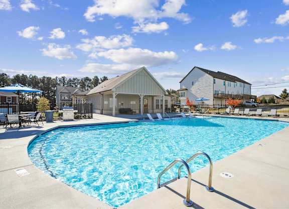 A large swimming pool in front of a building with a blue sky and clouds in the background.