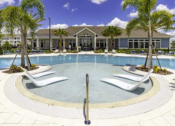 a large swimming pool with white chairs and a building in the background