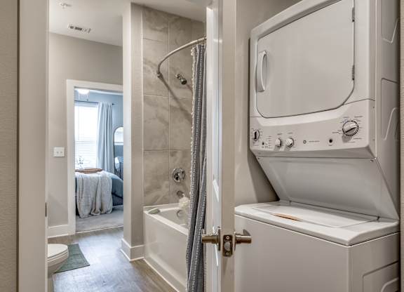 A white washing machine is in a bathroom next to a shower.