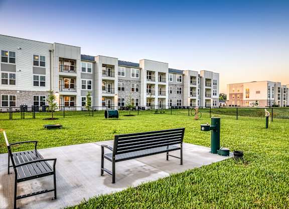 A park with benches and grass in front of apartment buildings.