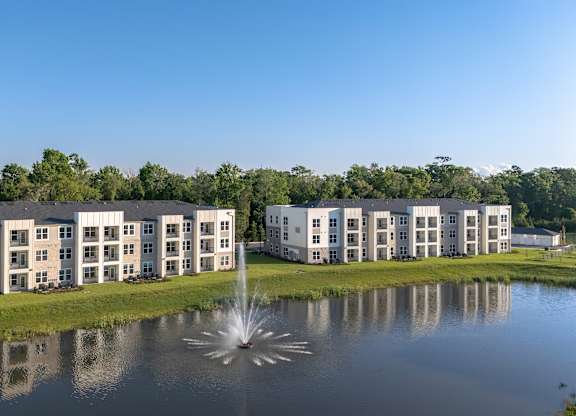 A fountain in the middle of a pond in front of a building.