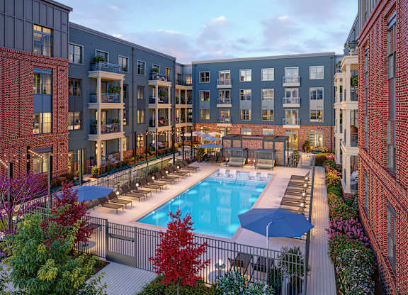 A pool surrounded by lounge chairs and umbrellas is surrounded by apartment buildings.