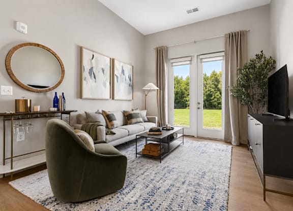 A living room with a grey couch, a round mirror, a coffee table, and a flat screen TV.