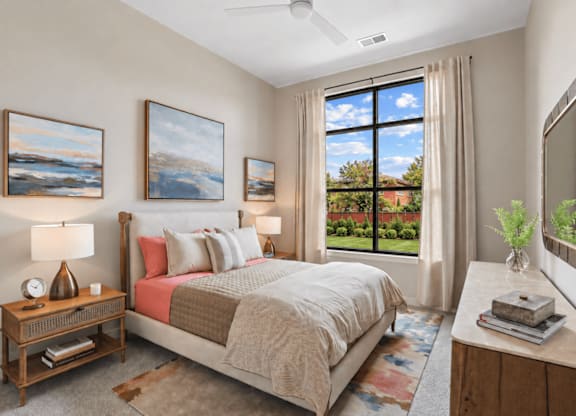 A bedroom with a large bed, a ceiling fan, and a view of the backyard through the window.