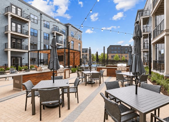A patio with tables and chairs is surrounded by apartment buildings.