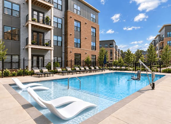 A pool surrounded by lounge chairs in front of apartment buildings.