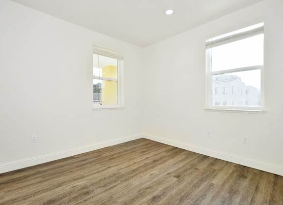 an empty room with wood floors and two windows