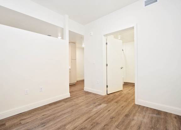 A room with white walls and wood flooring with a door on the right.