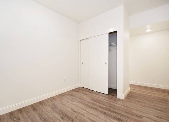 a bedroom with white walls and wood flooring and a closet