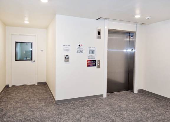 A hallway with a door on the left and an elevator on the right.