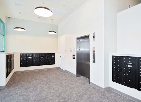 A hallway with a silver elevator and black lockers.