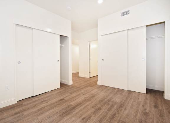 A room with white walls and wooden flooring with three white doors.