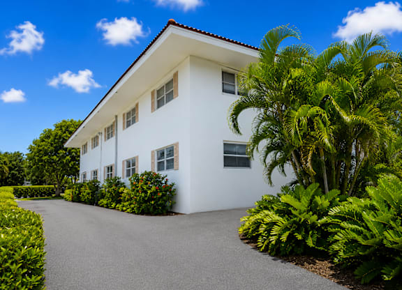 A white house with a driveway and green plants.