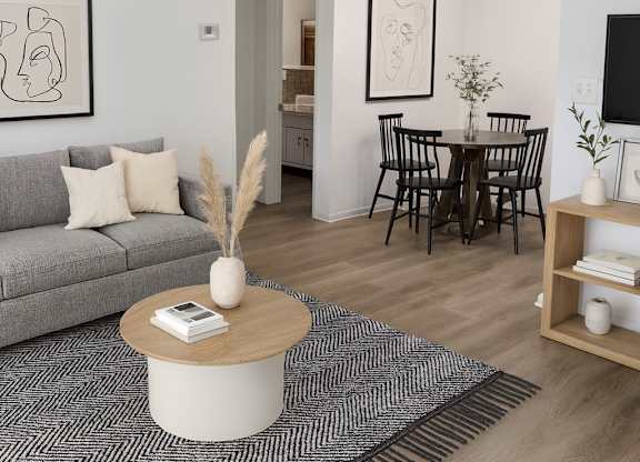 A living room with a grey sofa, a coffee table, a dining table with chairs, and a TV on the wall.