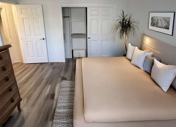 A bedroom with a bed, dresser, and a plant.