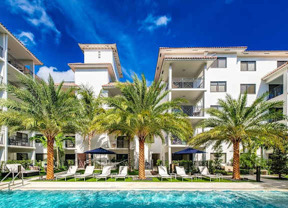 a large swimming pool in front of a hotel with palm trees