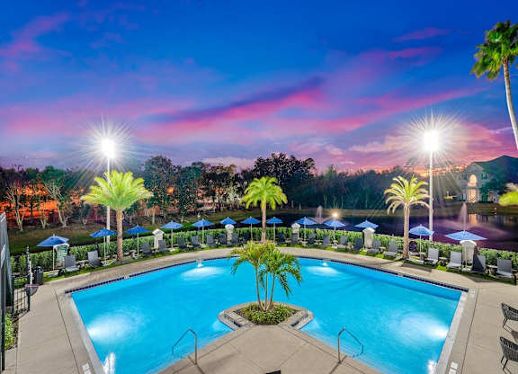 a swimming pool at night with palm trees and umbrellas
