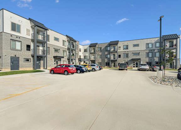 A red car is parked in a parking lot in front of a building.