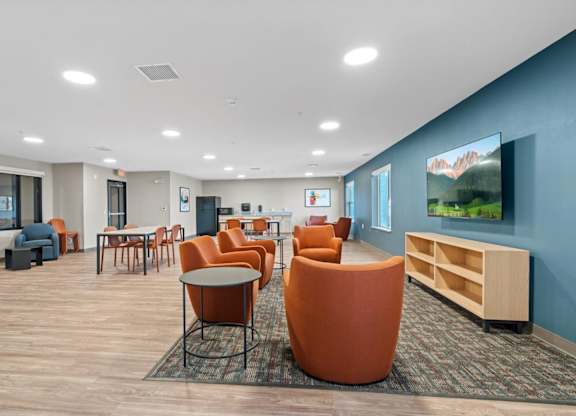 A spacious room with orange chairs and a television on the wall.