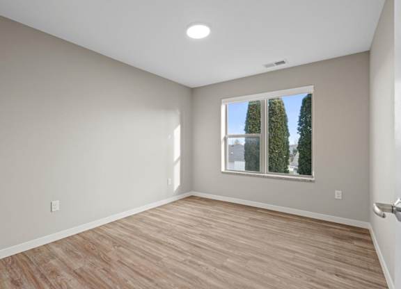 A room with wooden flooring and a window showing trees outside.