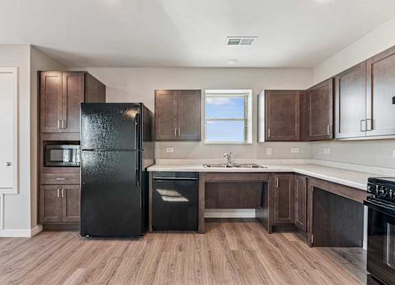 A black fridge stands in a kitchen with wooden floors and brown cabinets.