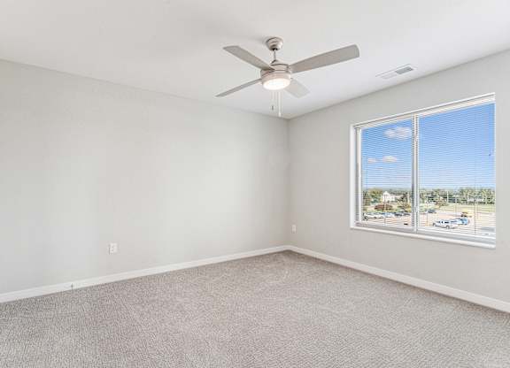 A room with a ceiling fan and a window overlooking a parking lot.