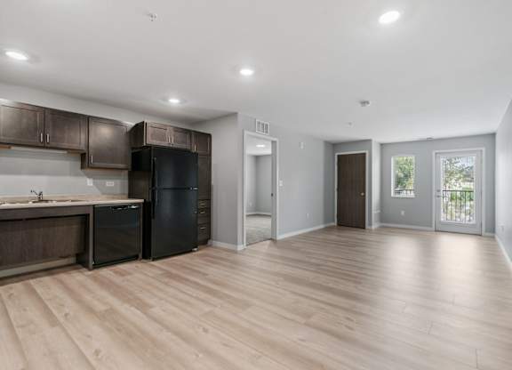 an empty kitchen and living room with wood flooring and black appliances