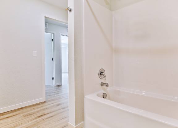 A white bathroom with a tub and a doorway to another room.
