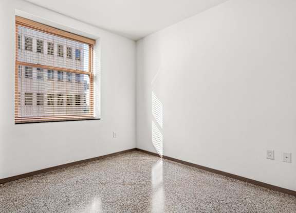 A room with a window covered in blinds and a tiled floor.