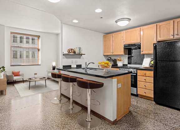 A kitchen with a black refrigerator, white countertops, and wooden cabinets.