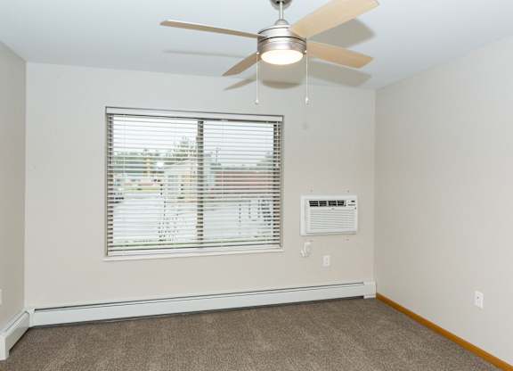 A room with a ceiling fan and a window with blinds.