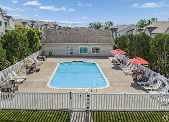 A pool surrounded by a white fence and chairs.
