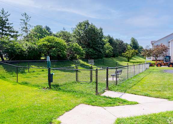 A park with a fence, bench, and greenery.