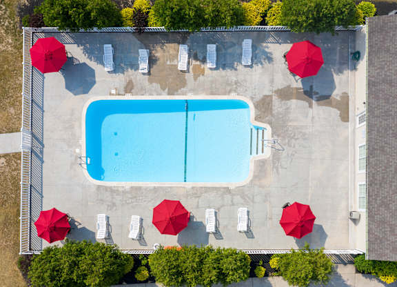 An aerial view of a pool surrounded by red umbrellas and trees.