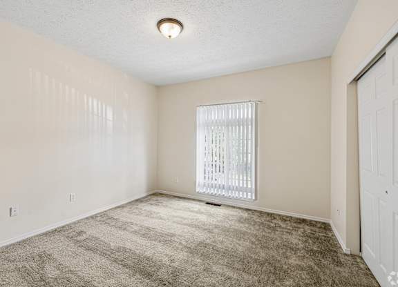 A room with a carpeted floor and a window with blinds.