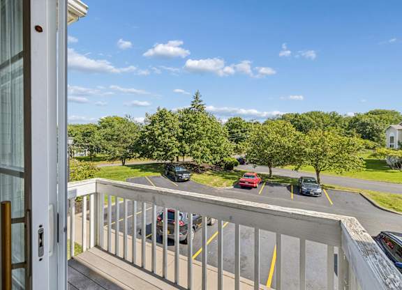 A view from a balcony looking out at a parking lot and trees.