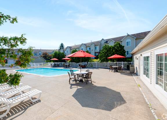A pool area with chairs and umbrellas in front of a row of houses.