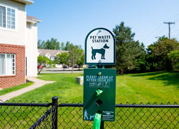 A sign for a pet waste station is displayed on a fence.
