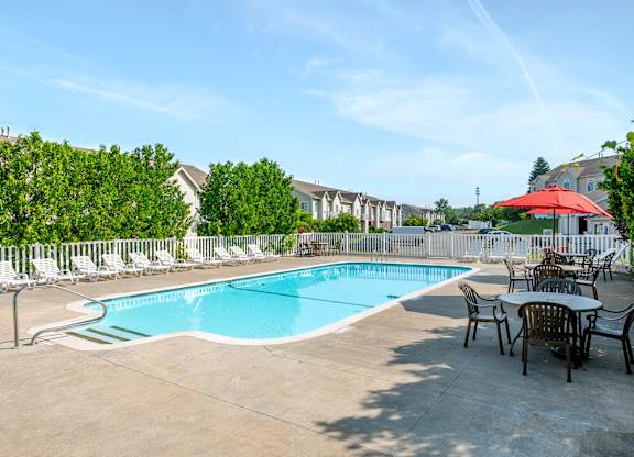 A pool surrounded by chairs and trees.