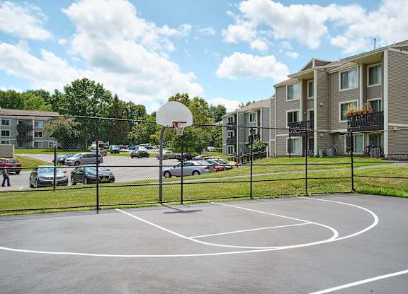 A basketball court is surrounded by a black fence and apartment buildings.