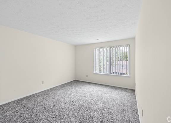 A room with a carpeted floor and a window with blinds.