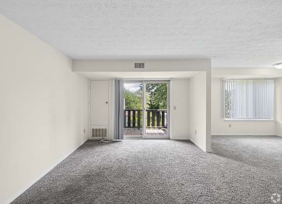 A spacious room with a carpeted floor and a sliding glass door leading to a balcony.