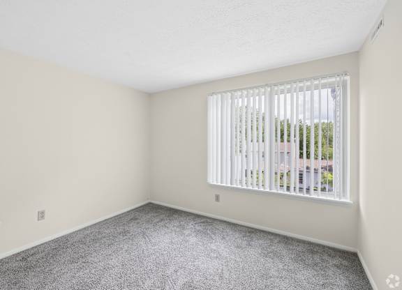 A room with a carpeted floor and a window with blinds.