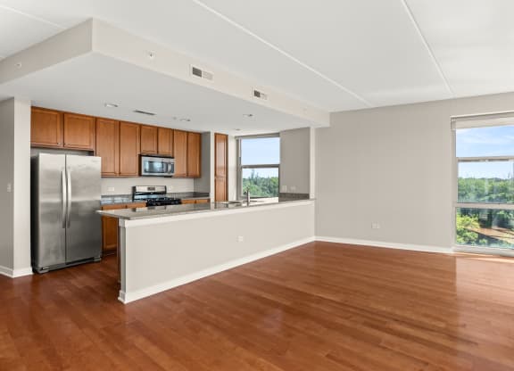 an empty living room with a kitchen and a stainless steel refrigerator