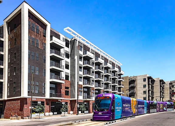A purple train is on the tracks in front of a building.