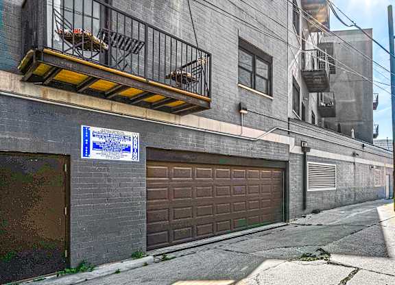 A blue and white sign is on a pole in front of a closed brown garage door.