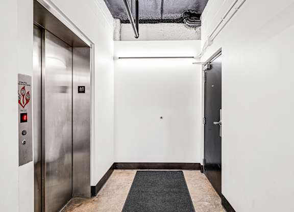 A hallway with a silver elevator on the left and a closed door on the right.