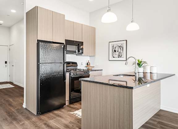A modern kitchen with a black fridge and wooden cabinets.