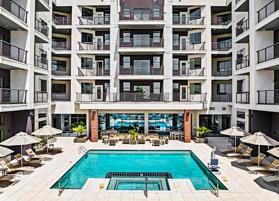 A large swimming pool in the middle of a courtyard surrounded by chairs and umbrellas.