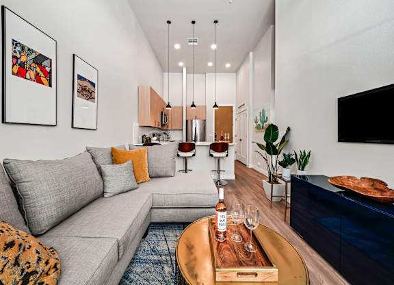 A modern living room with a grey sofa, a wooden coffee table, and a TV on the wall.